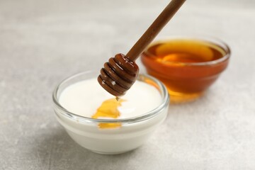 Dripping honey into Greek yogurt at light grey table, closeup