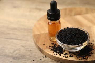 Black cumin seeds and oil on wooden table, closeup. Space for text