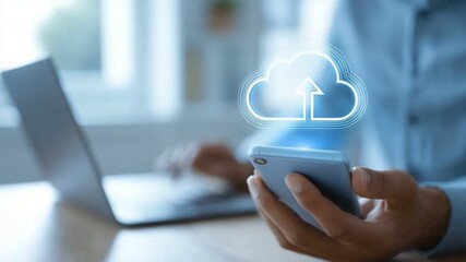 A person uploads files to the cloud using a smartphone while working on a laptop. The image represents modern technology and the convenience of digital storage solutions. - Powered by Adobe
