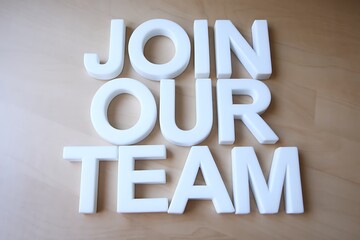 "Join Our Team" is prominently displayed in large, white, three-dimensional letters on a plain, light brown or beige surface, creating an inviting message for prospective employees.