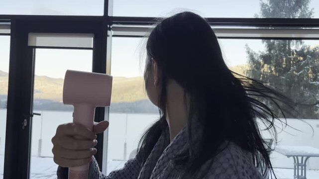 Adult woman drying her hair with a pink hair dryer at home, part of a daily beauty routine and hair care process, modern self-care, grooming habits, and healthy hair maintenance in a cozy home interio