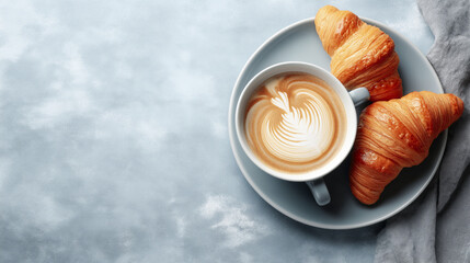 Warm latte with delicate foam art served on a gray plate beside two golden croissants