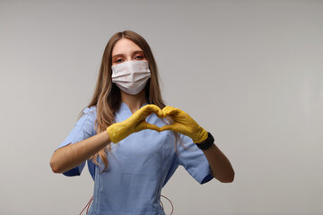 Young caucasian female nurse wearing protective mask and gloves making heart gesture