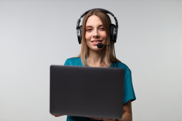 Caucasian young female professional with headset holding laptop in virtual meeting