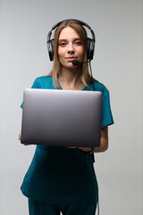 Female caucasian young adult in teal outfit holding laptop with headset