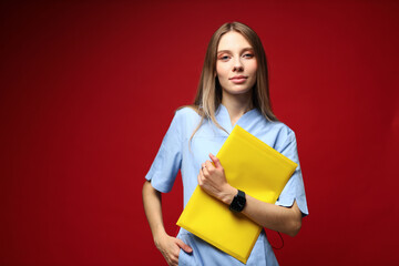 Confident young caucasian female nurse holding yellow folder against red background
