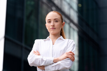 Professional young woman in white shirt poses confidently outside modern glass buildings in a city setting