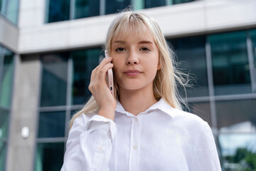 Fototapeta premium Young woman making a call outside a modern building on a sunny day in the city