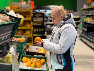 A woman inspecting bell peppers in a grocery store, surrounded by fresh produce
