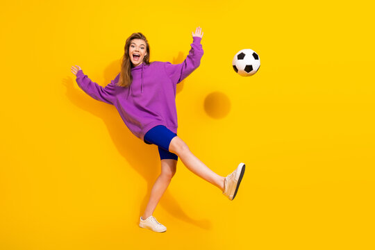 Young woman in purple hoodie kicks soccer ball against bright yellow background for a playful sporty lifestyle image