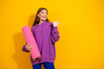 Young woman in purple hoodie holds pink yoga mat smiles against bright yellow background for casual lifestyle stock photo featuring fashion and sporty vibe
