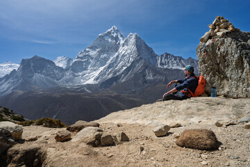 Hiker resting by cairn viewing Ama Dablam peak on Everest Trek, Nepal