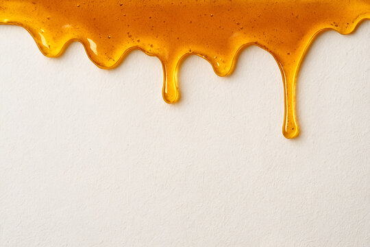Thick golden honey or caramel syrup dripping down on a clean white background sweet dessert ingredient