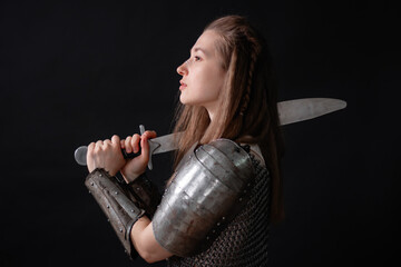 Obraz premium Portrait of a young woman, fantasy warrior in armor with a sword in her hands isolated on a dark background.