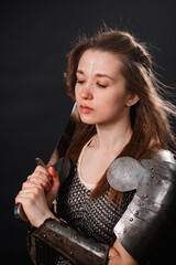 Obraz premium Portrait of a young woman, fantasy warrior in armor with a sword in her hands isolated on a dark background.