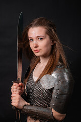 Obraz premium Portrait of a young woman, fantasy warrior in armor with a sword in her hands isolated on a dark background.