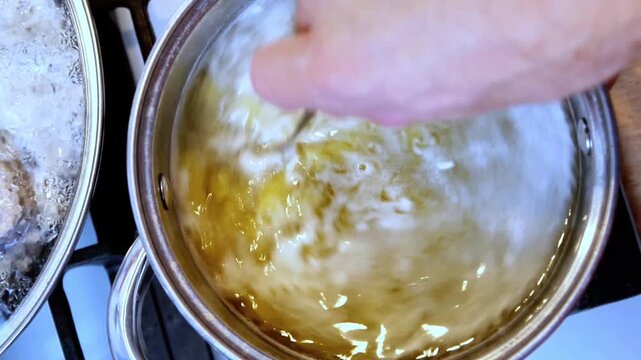 Close up top view pasta stirred with spoon in pot creating water vortex boiling cooking process transparent water home kitchen preparation
