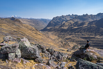 Hiker resting on ridge overlooking Lares Valley and town, Peruvian Andes