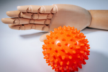 Obraz premium A wooden mannequin's hand is behind a bright orange, sharp massage ball on a smooth surface with soft lighting.