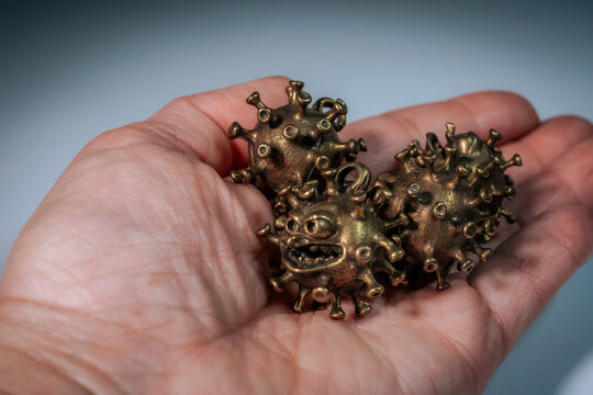 A person gently holds four small bronze-colored virus-like figures with cartoon faces in their palms.