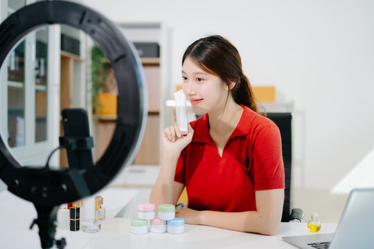 Asian beauty influencer filming skincare review with ring light, showcasing cosmetic jars and products for online content, beauty marketing, and social media promotions.