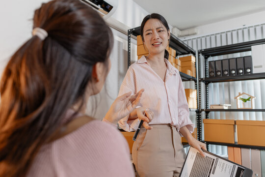 Two young women working together in a small business office, organizing packages, reviewing documents, and planning tasks with smiles. Scene reflects teamwork, productivity and modern entrepreneurship