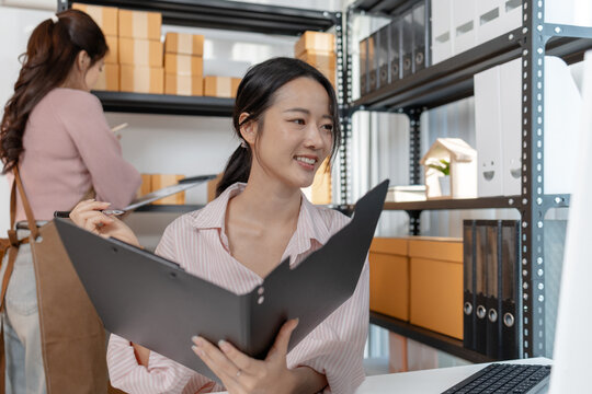 Two young women working together in a small business office, organizing packages, reviewing documents, and planning tasks with smiles. Scene reflects teamwork, productivity and modern entrepreneurship
