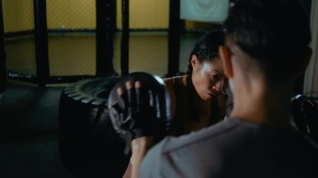 Japanese woman boxing with a coach holding pads, demonstrating clean technique and professional focus during an intense training session in the gym.