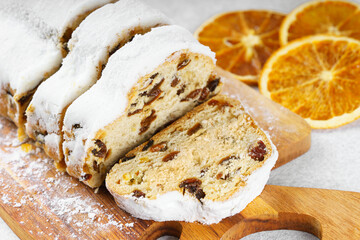 Traditional Christmas stollen, sweet fruit loaf sliced on wooden board, dusted with powdered sugar on white textured background. Spices, dried fruits and festive decorations create winter holiday mood