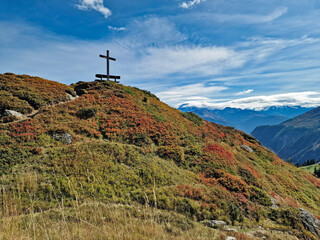 Autumn hill with heather, wooden bench and large wooden cross on top, overlooking the Swiss Alps in the Belalp region, Bruchegg, Naters, Switzerland.