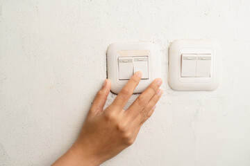 Close up of a hand touching a white light switch on a speckled wall
