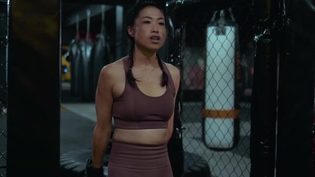 Confident Japanese woman enters the MMA cage, warming up and staring at her opponent with focus and determination before the fight begins or training.