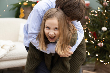 Siblings having fun together in a cozy holiday setting with a decorated Christmas tree