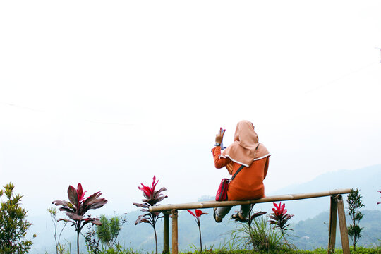 Woman in hijab enjoying nature view sitting on bamboo fence outdoors