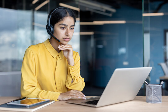 Serious and thoughtful young Indian woman in a headset is in the office and working intently on a laptop