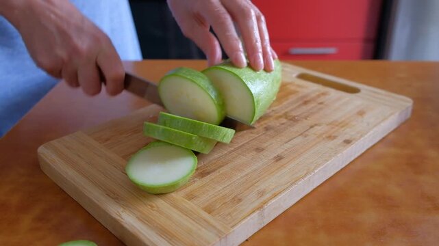 A person and a woman cutting zucchini on a board and table, hand movements visible. Healthy eating product. slicing a cucumber