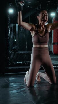 Vertical shot of a female MMA fighter celebrating victory in the cage, smiling and raising her arms, a powerful moment of joy, success and positive emotion.