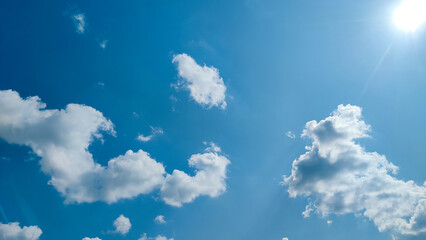 Bright blue sky with white cumulus clouds and visible sun flare