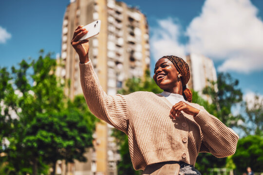 Young happy Black woman is taking selfie on sunny day with her smartphone. - Powered by Adobe