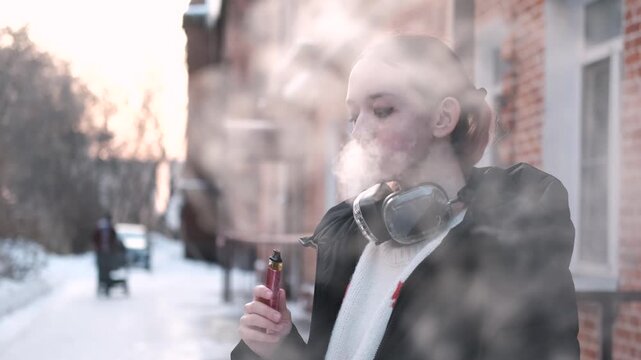 Teen vaper. A young girl smokes an electronic cigarette outside in winter. Close-up.