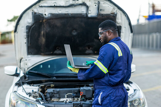 African mechanic using a laptop to run diagnostics on a car engine, troubleshoot issues, and monitor vehicle performance in his workshop