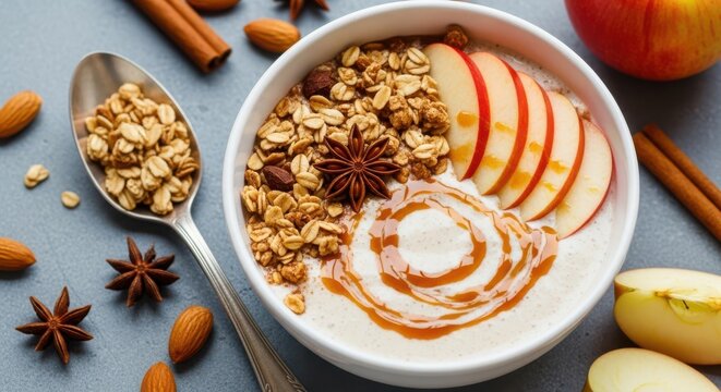 Healthy breakfast bowl with yogurt, granola, apple slices, caramel drizzle, cinnamon, star anise, and almonds on a dark background