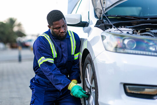 African mechanic in blue overalls changing a car tire in his workshop