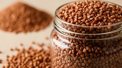 Close up of raw buckwheat groats in a glass jar with a pile of buckwheat in the background