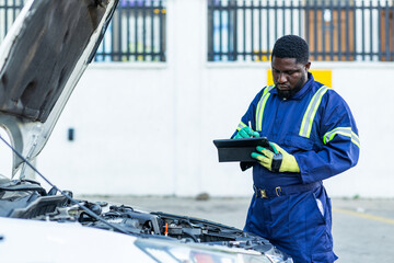 African mechanic using a smart tablet to record car diagnostics during routine maintenance in his workshop