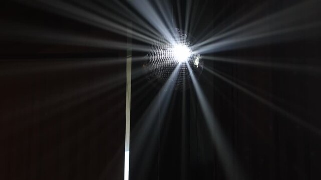 Disco ball with reflected moving rays rotating at nightclub. Searchlight illuminates of spinning mirror disco ball, white light reflection on walls and ceiling. Party celebration concept