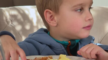 side angle child in denim blue top eating puree little spoonfuls slow natural behavior everyday home kitchen moment Concept of real family mealtime and natural childhood routine - Powered by Adobe