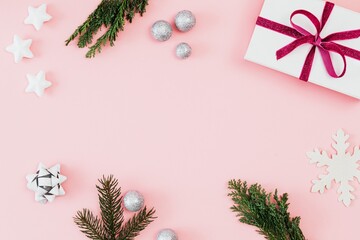 A Christmas pink background with ornaments, gift box and tree leaves.