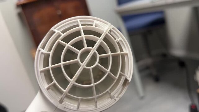 A macro close-up shot focusing on the intake grille and internal fan mechanism of a handheld hair dryer. The scene highlights hair care, hygiene, and domestic electrical appliances.
