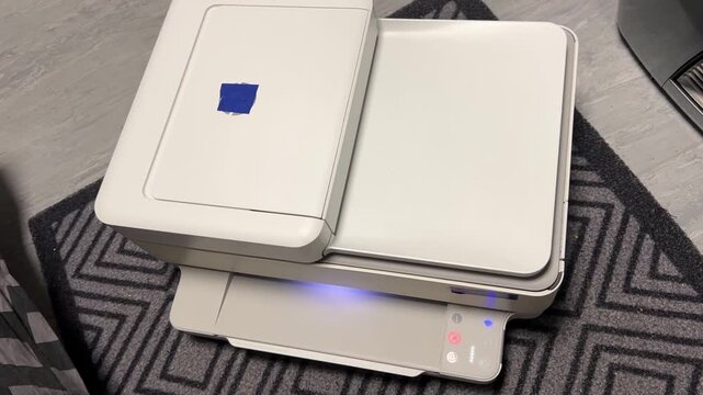 A close-up shot of a modern multifunction household printer feeding a clean sheet of paper from the output tray. The scene highlights home office work and printing technology.